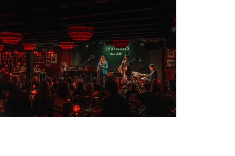 A band on stage performing at Ronnie Scott's Jazz Club in London with an audience watching.